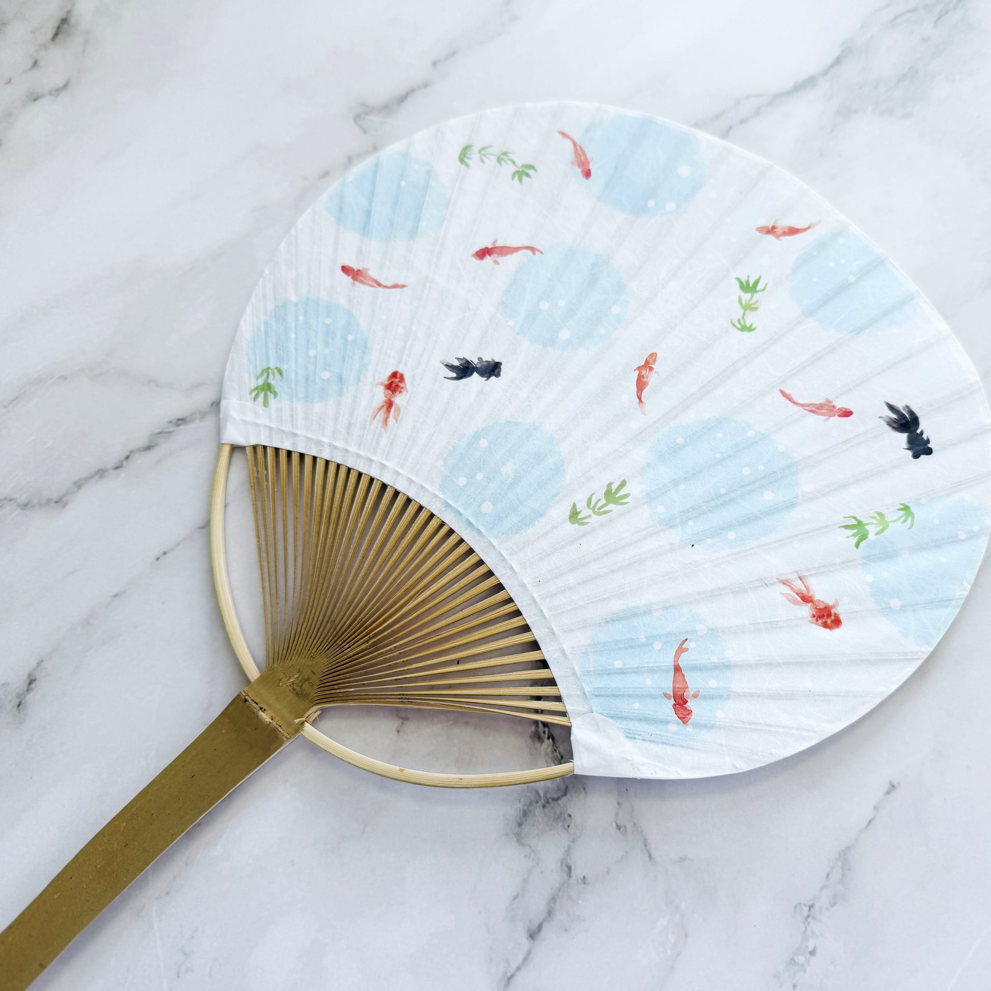 Handheld fan with gold handle and decorative paper design on a marble surface