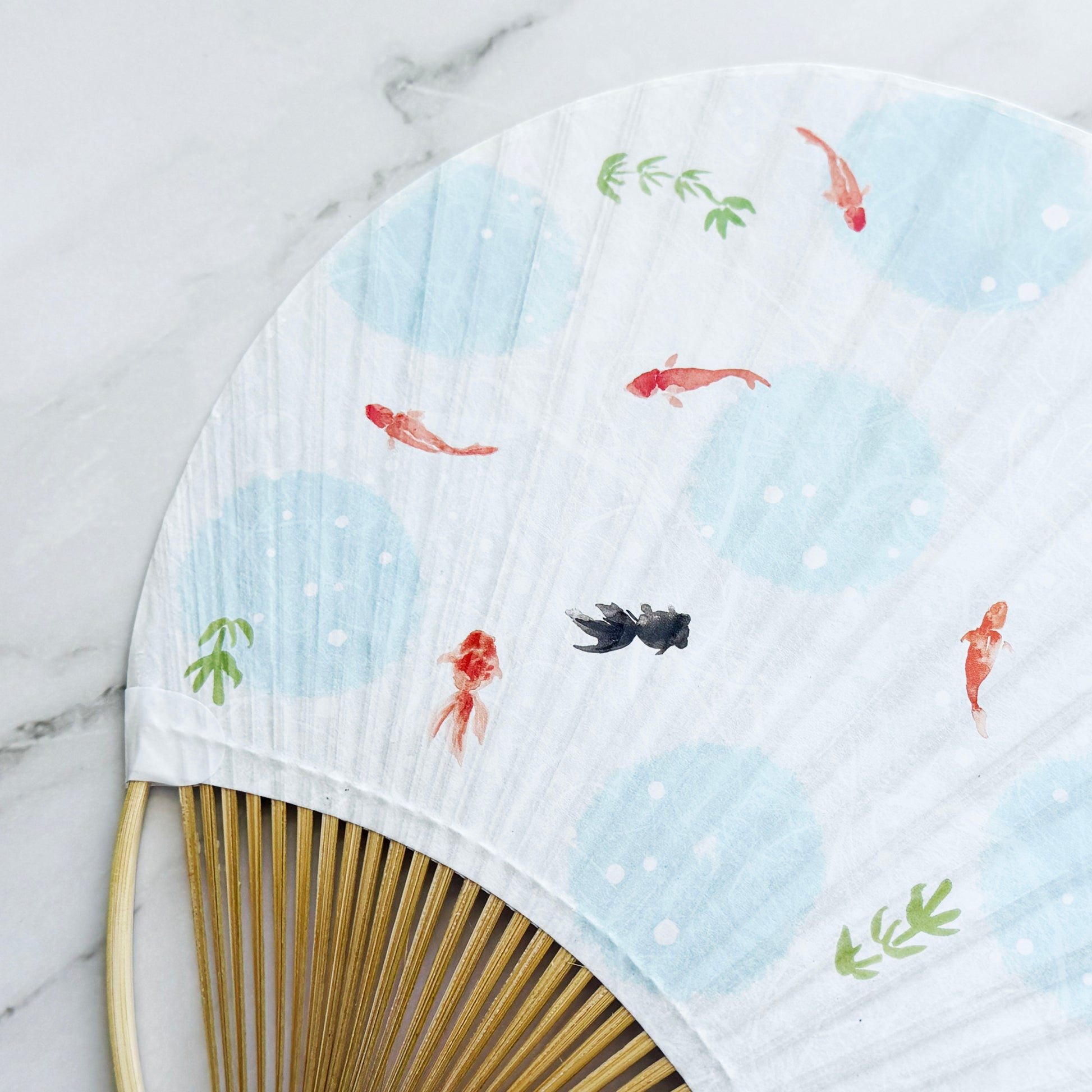 Handheld fan with fish design on a marble surface
