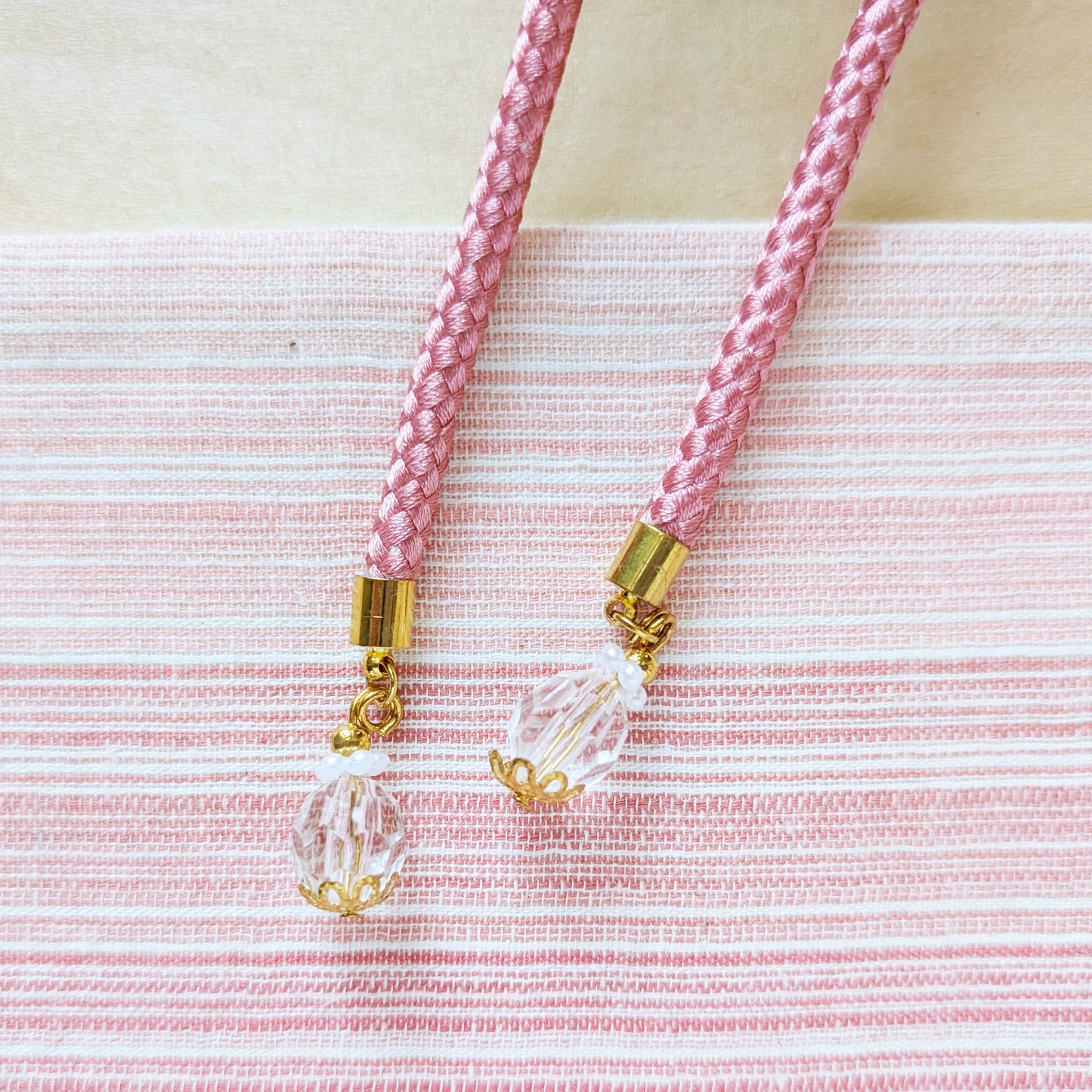 Pink braided cord with gold accents and clear beads on a pink and white striped background