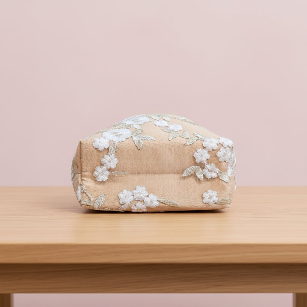 Beige cosmetic bag with floral embroidery on a wooden surface and pink background