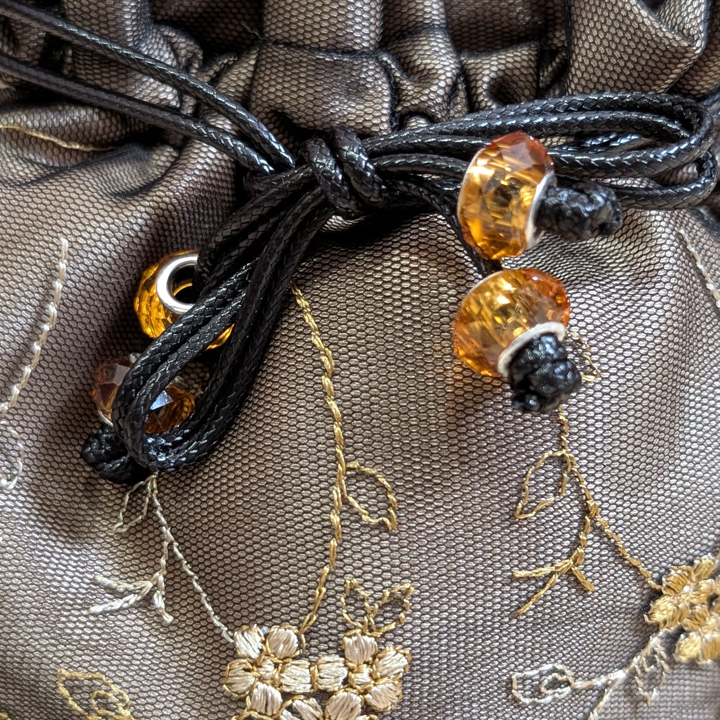 Close-up of a black cord with amber beads on a textured fabric background